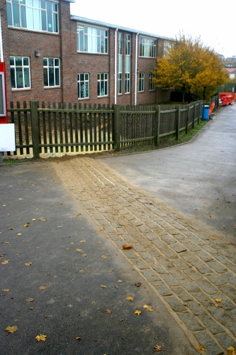 Granite sett flow diverter comprising combined channel and hump in a wale-like formation.  The channel intercepts overland flow and diverts it to the raingarden basins beyond the fence (shown during construction).